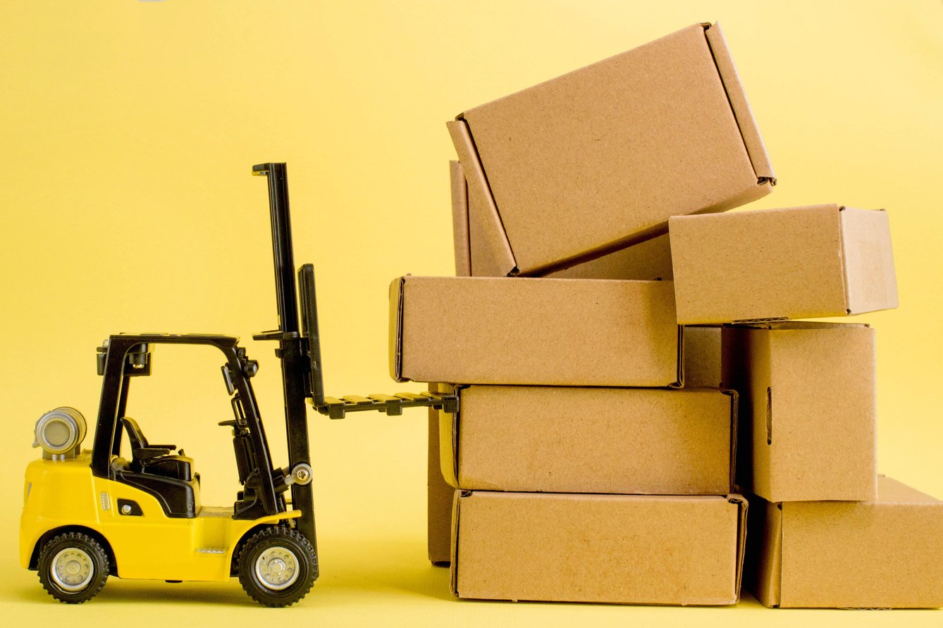 Forklift truck raises cardboard boxes on a yellow background. Cargo sorting concept